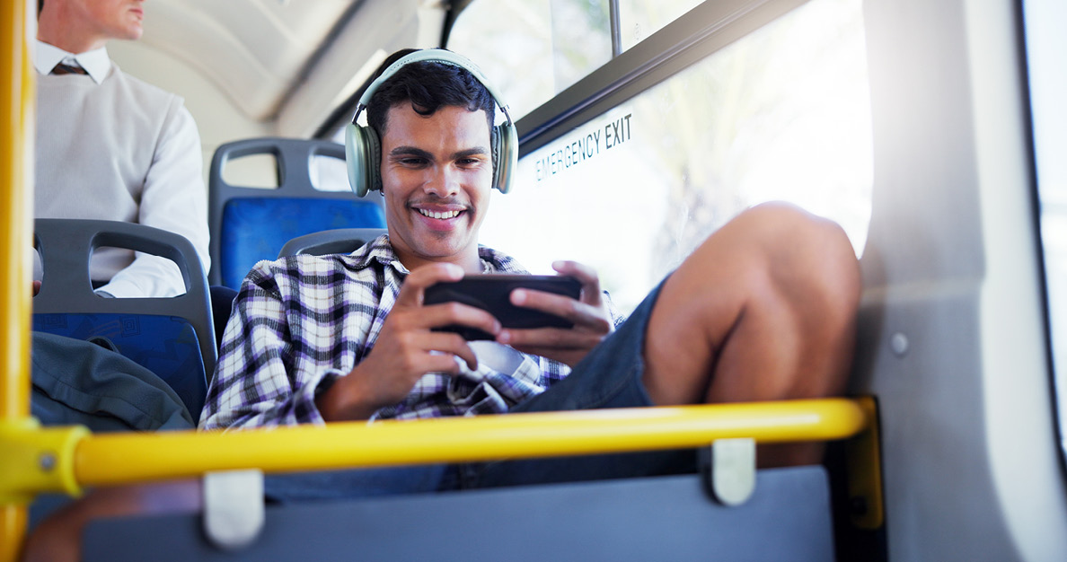 Young man enjoying 5G mobile gaming on smartphone with headphones while riding the bus.
